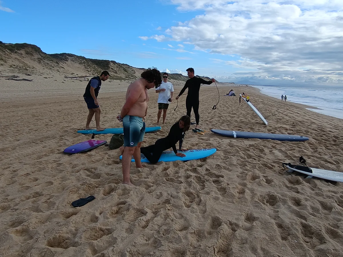 The team practising on surfboards on the sand beside the ocean.